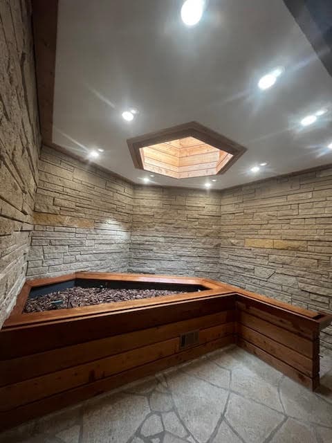 Stacked stone walls surround a wooden planter beneath a recessed ceiling with a hexagonal skylight.