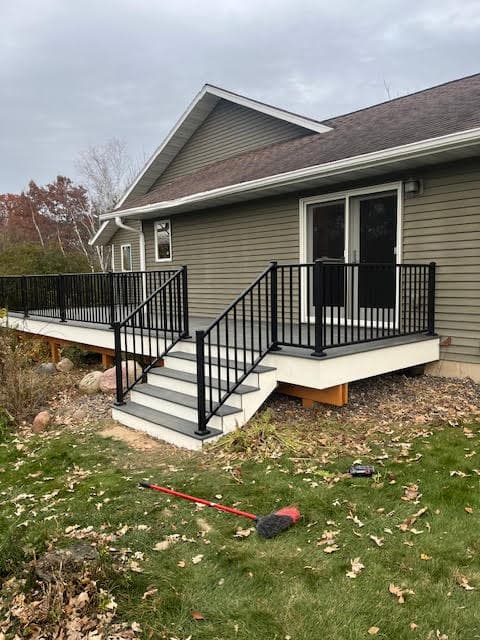 Grey composite deck with black metal railings and stairs on a house with green siding.