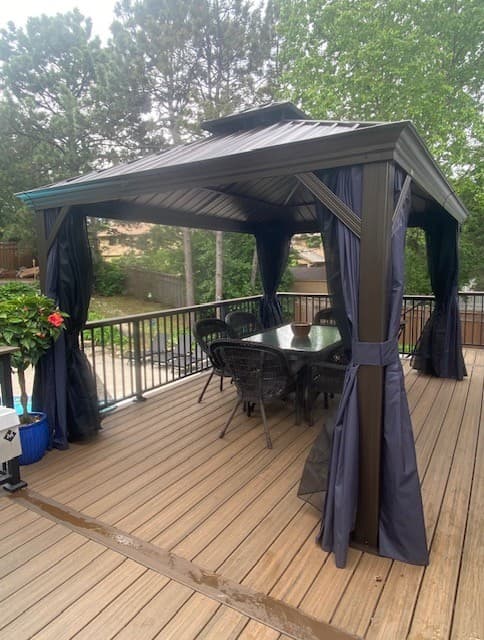 Bronze metal gazebo with curtains and a dining set on a spacious wooden deck.