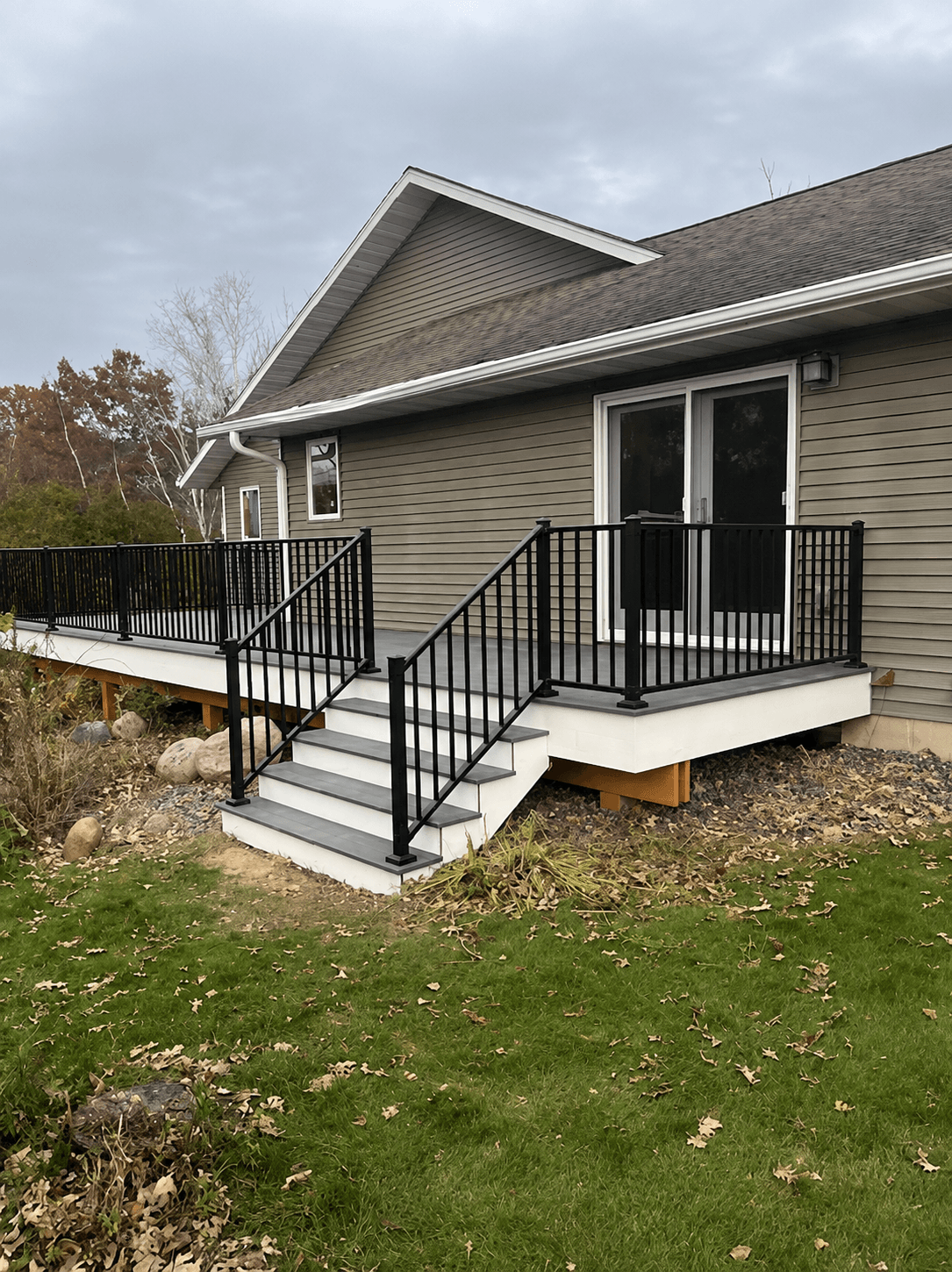 Modern grey deck with black metal railings and white stairs attached to a tan house.