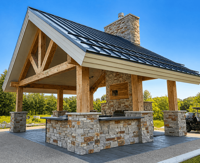 Outdoor kitchen pavilion with stone pillars, timber beams, and a dark metal gabled roof.