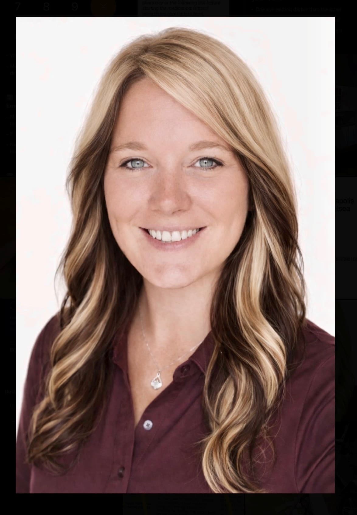 Smiling woman with long, wavy blonde and brown hair wearing a maroon button-down shirt.