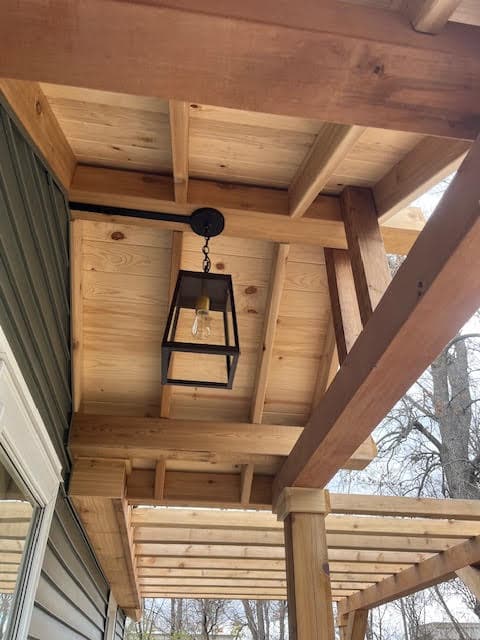 Black metal lantern hanging from a light wood ceiling with exposed beams on an outdoor porch.