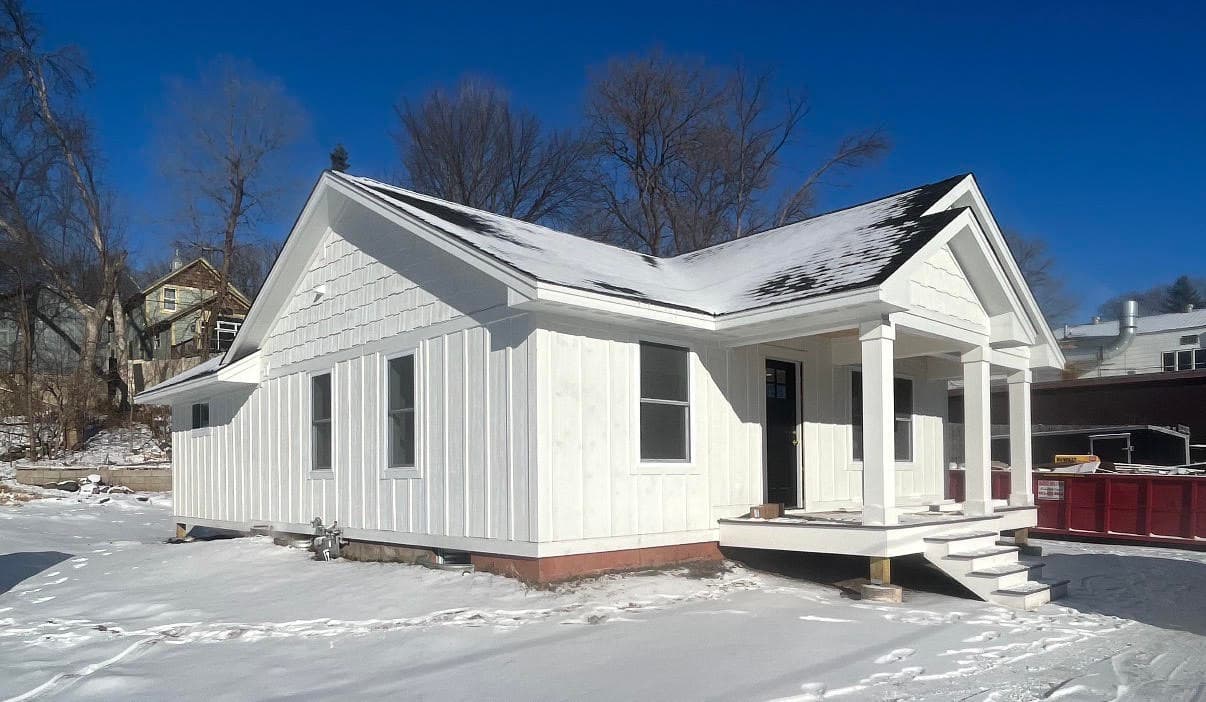 White board and batten house with a front porch on a snowy lot under blue sky.