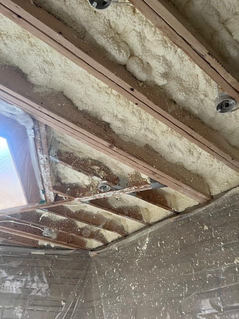Thick spray foam insulation applied between wooden ceiling rafters in a room under construction.