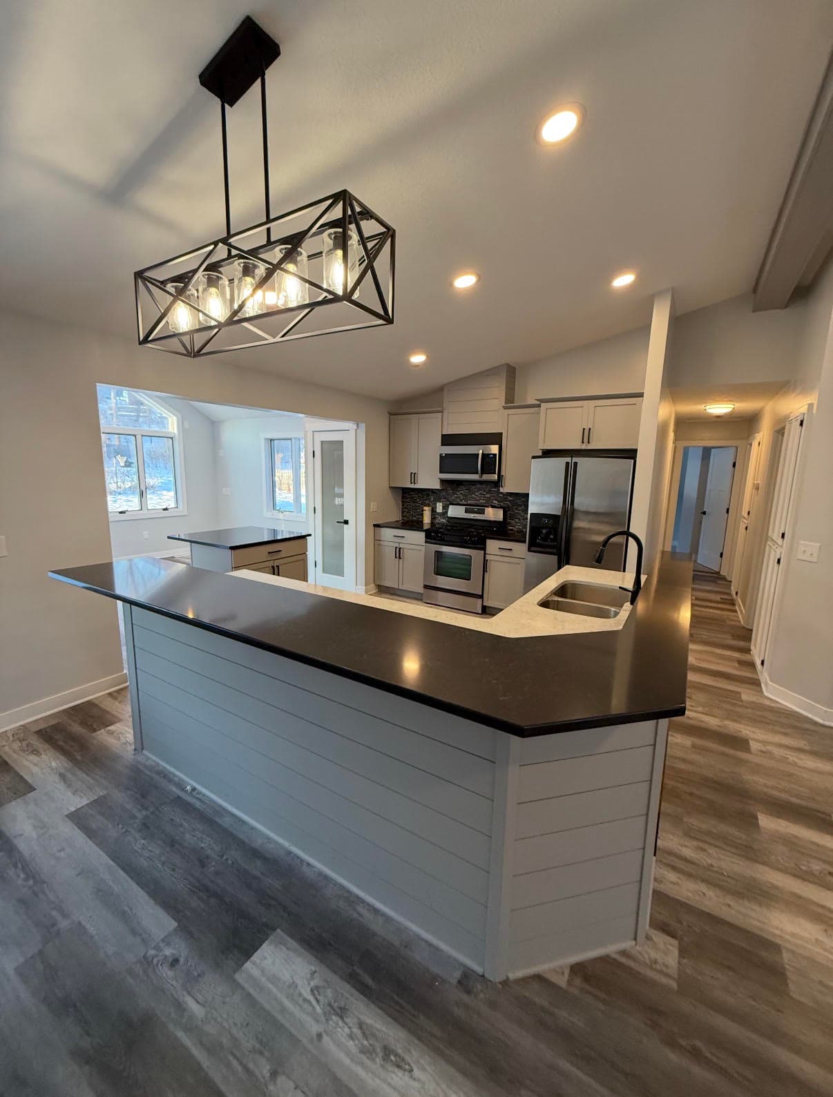 Modern kitchen with gray cabinets, stainless steel appliances, and a large island with black chandelier.