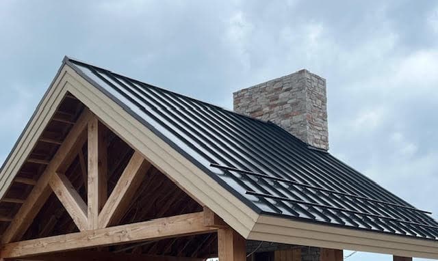 Black standing seam metal roof with snow guards on a timber frame with stone chimney.
