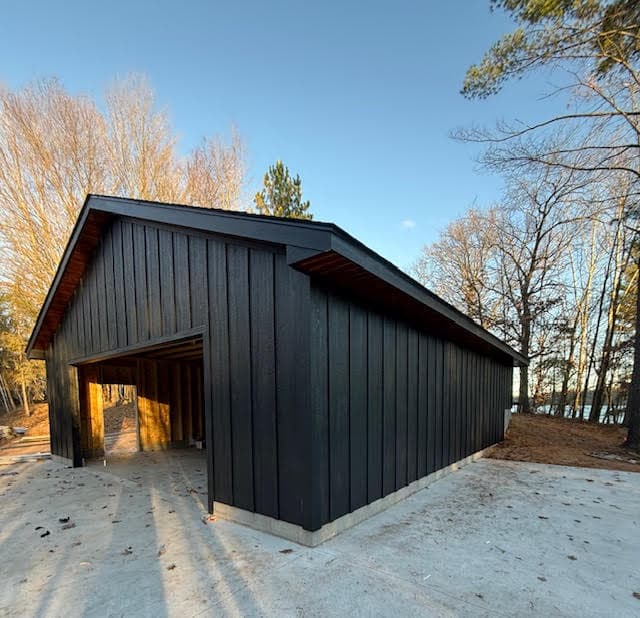 Modern black garage with vertical siding and wood soffits on a concrete slab near trees.