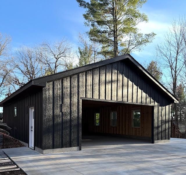 Modern black garage with textured vertical siding and an open bay door on concrete.
